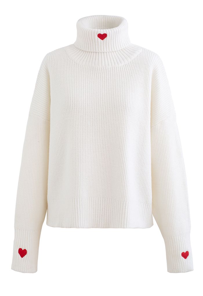 Front view of a cozy white turtleneck crop sweater with embroidered red hearts on the neck and sleeves.