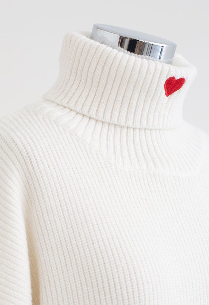 Close-up of the turtleneck with a red heart embroidery on a white sweater, highlighting its romantic charm.