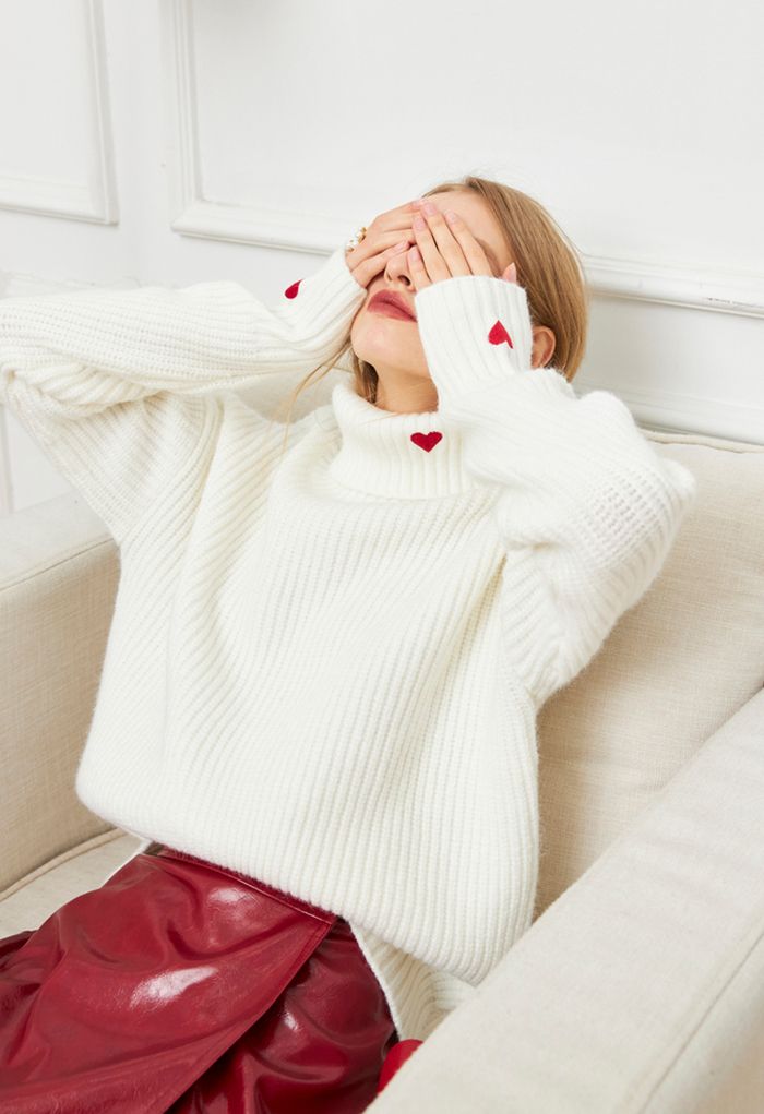 A playful scene with a model wearing a white turtleneck sweater, covering her face, featuring red heart details.