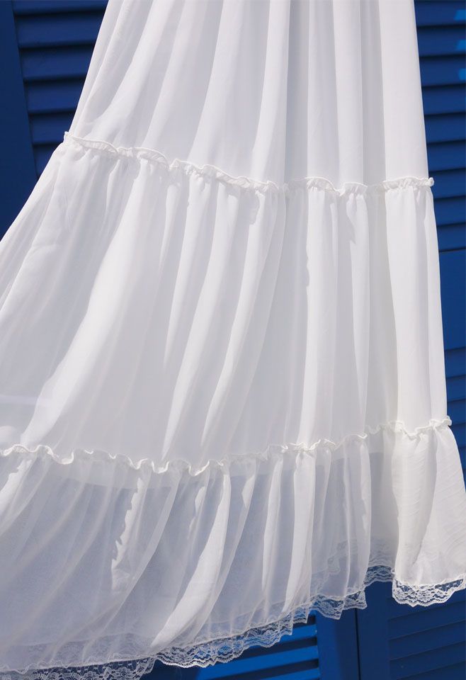 Detail shot of the flowing white chiffon fabric with lace trim of a summer maxi dress, set against a blue shutter.