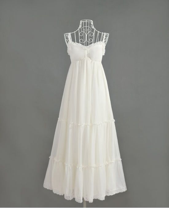 Front view of a white maxi chiffon dress with tiered layers and lace accents, displayed on a wire mannequin against a gray background.