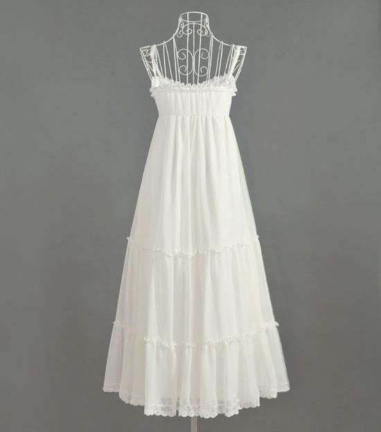 Back view of a soft white maxi chiffon dress with tiered layers, shown on a wire mannequin against a neutral gray backdrop.