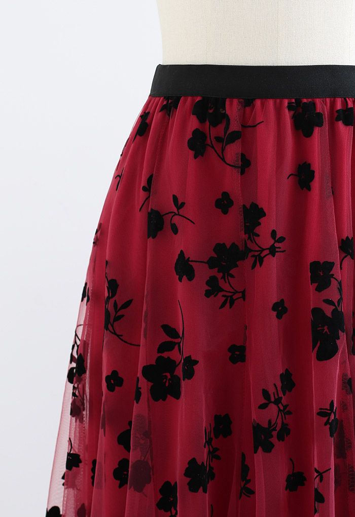 Detail shot of the waistline of a red 3D posy double-layered mesh midi skirt with black floral patterns.