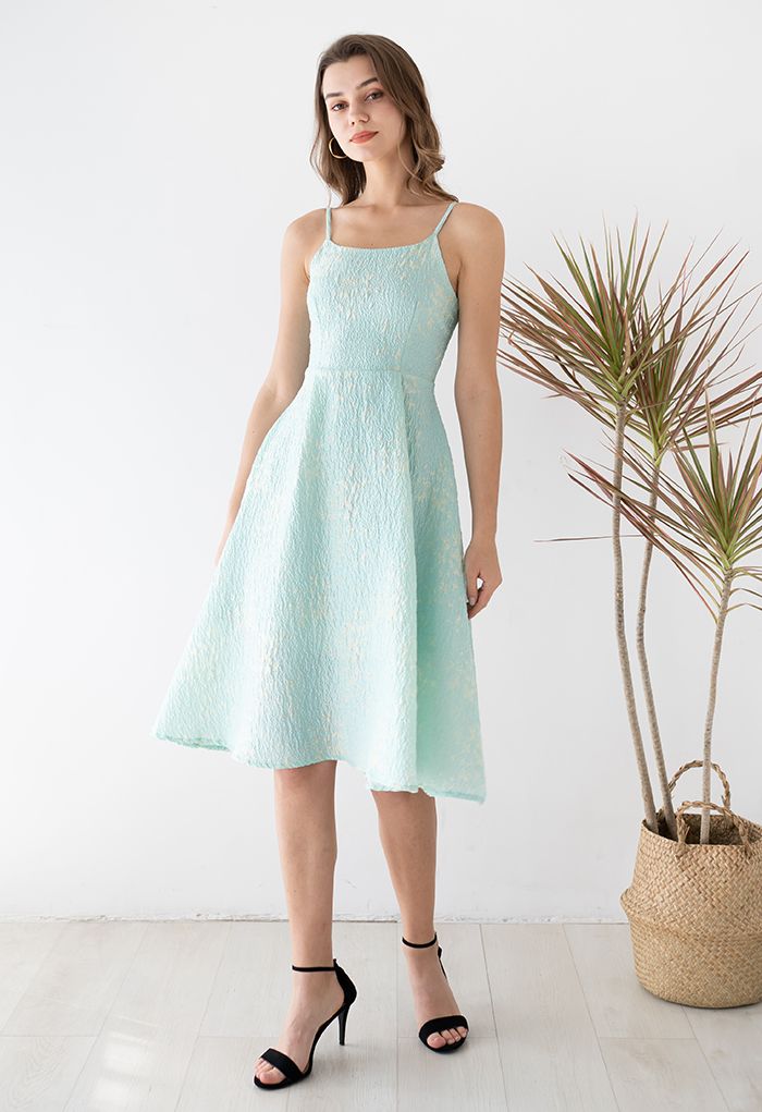 Model wearing the blue cami midi dress with butterfly embroidery, standing next to a plant in a bright room.