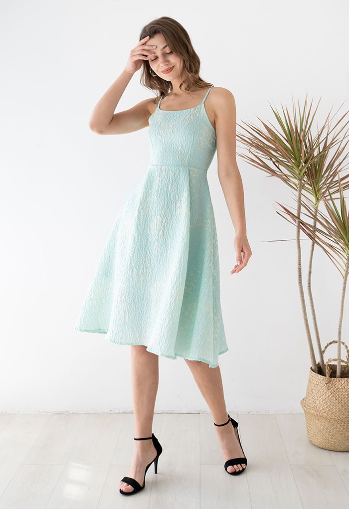 Model in a blue cami midi dress with butterfly embroidery, playfully touching her hair in a bright setting.