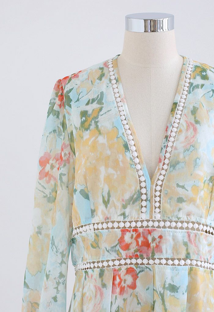 Detail shot of a floral long sleeve dress with a deep V-neck and intricate lace trim in soft yellow hues.