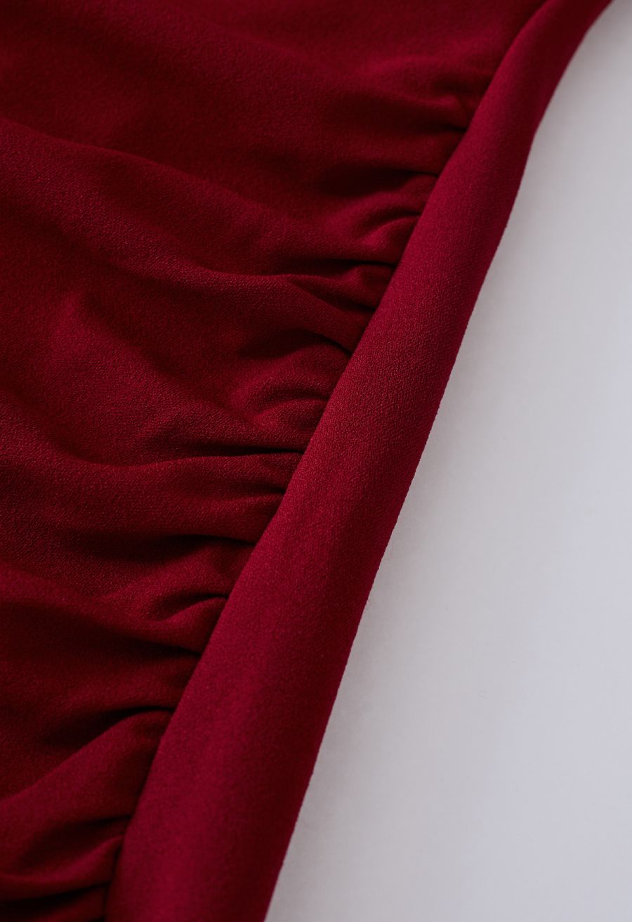 Detail shot of the ruched side on a burgundy dress, highlighting the rich fabric and elegant draping.