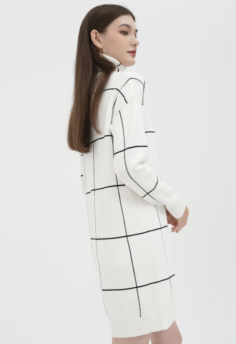 A woman in a white turtleneck sweater dress with a black grid pattern, captured in a side view, exuding a modern vibe.