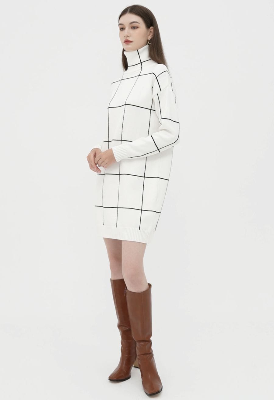 A woman wearing a white turtleneck sweater dress with a black grid pattern, standing in a relaxed pose, showcasing a chic style.