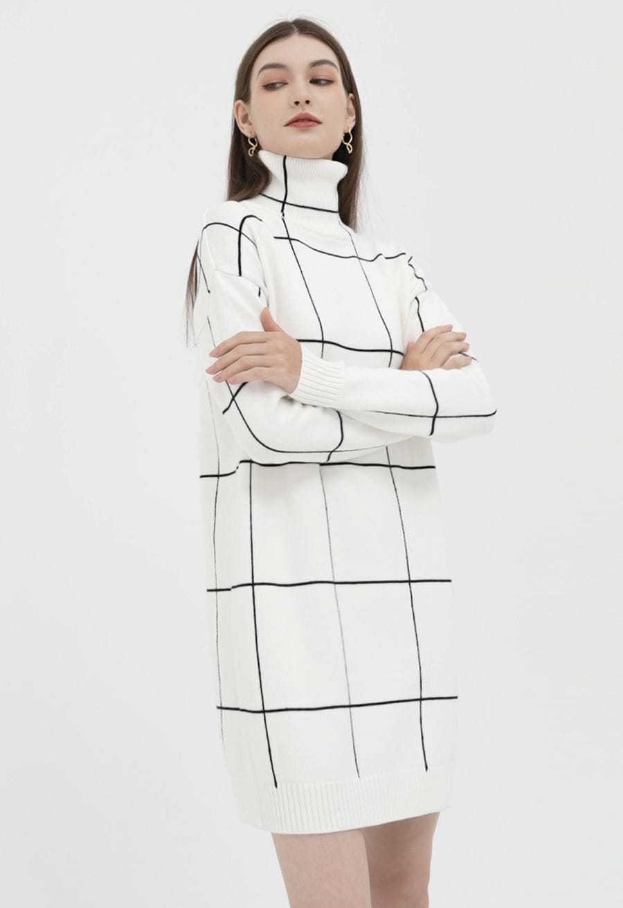 A woman wearing a cozy, white turtleneck sweater dress with a black grid pattern, shown in a front view.