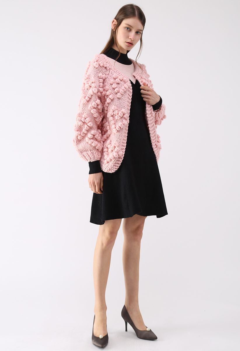 Front view of a model wearing a pink knit cardigan with textured details over a black dress, exuding a cozy and romantic vibe.