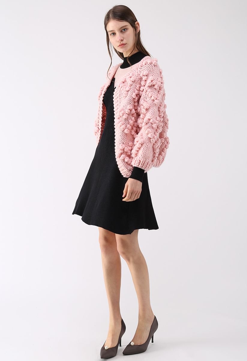 Front view of a model in a pink knit cardigan with bubble details paired with a black dress, giving a cozy and chic appearance.