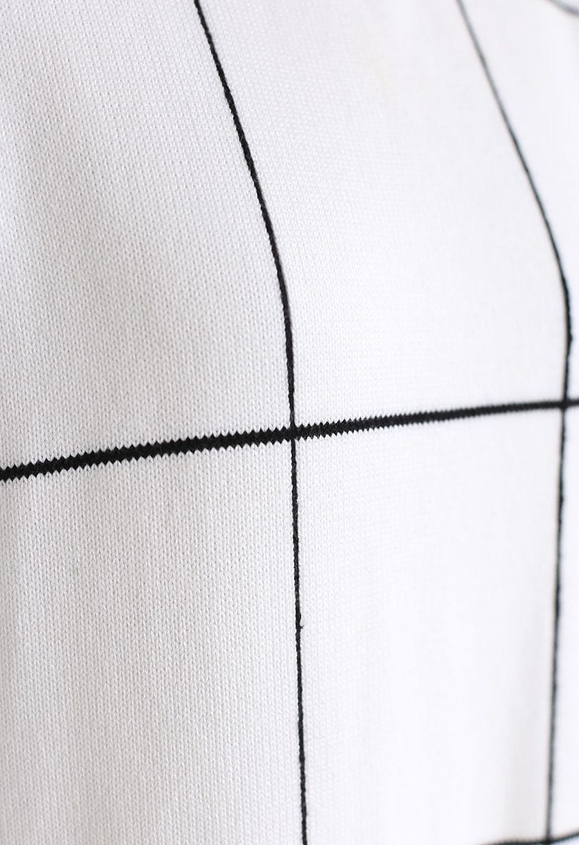 Close-up detail of a white sweater dress with a black grid pattern, highlighting the texture and design.