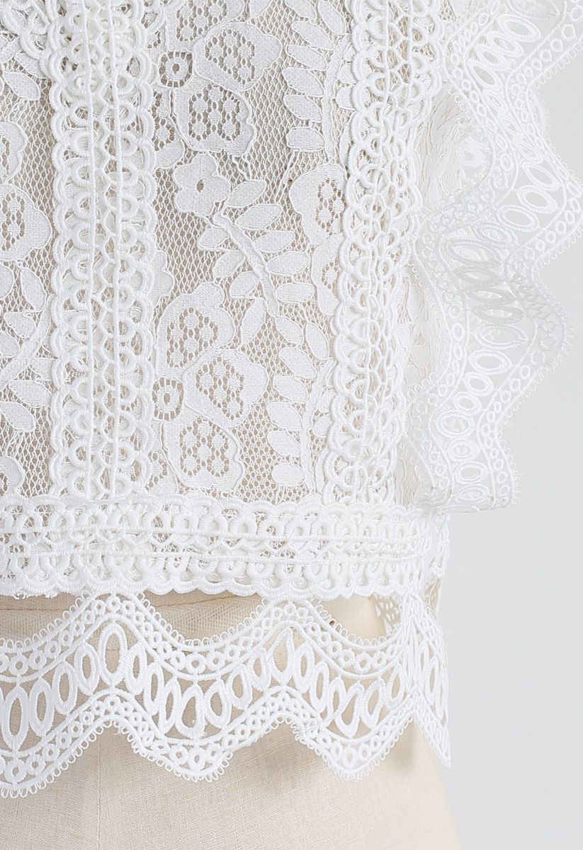 Detail shot of a white crochet lace top highlighting the intricate floral patterns and scalloped hem.
