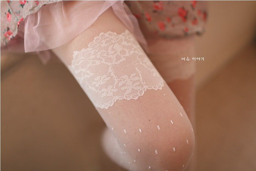 Detail shot of white tights featuring intricate lace design at the top and subtle dot pattern, exuding elegance and charm.